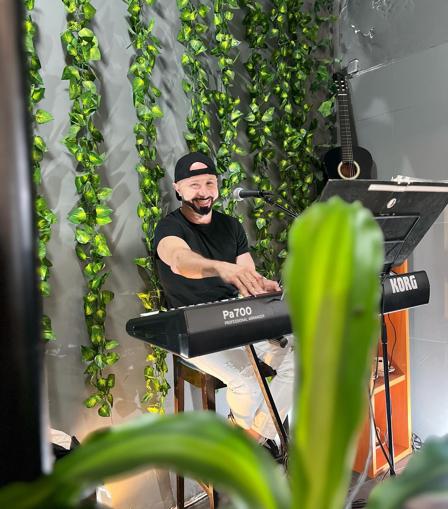 Músico a tocar teclado ao vivo junto a uma parede decorada com trepadeiras artificiais, na Churrasqueira do Marques